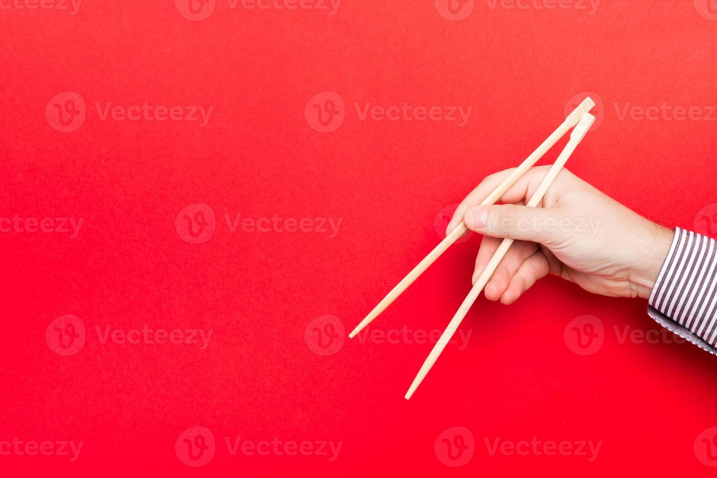 houten eetstokjes vastgehouden met mannetje handen Aan rood achtergrond. klaar voor aan het eten concepten met leeg ruimte foto