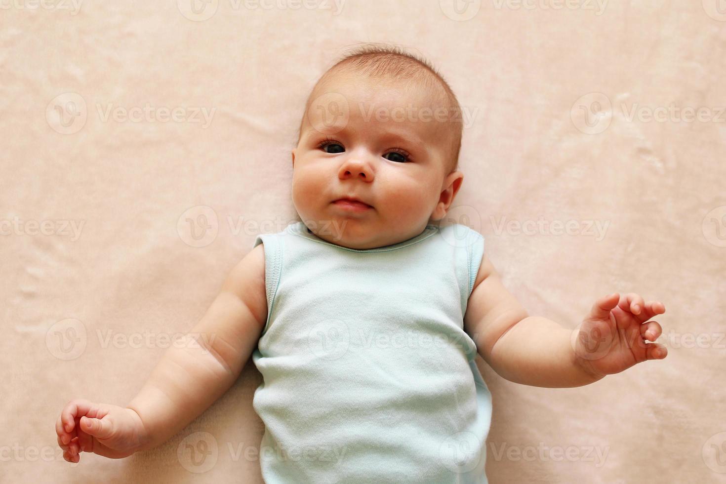 schattig drie maand baby in blauw bodysuit is aan het liegen Aan een beige deken en op zoek Bij de camera. foto