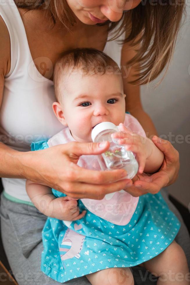moeder helpt haar dochter naar drinken water. kind leert naar houden een fles. foto