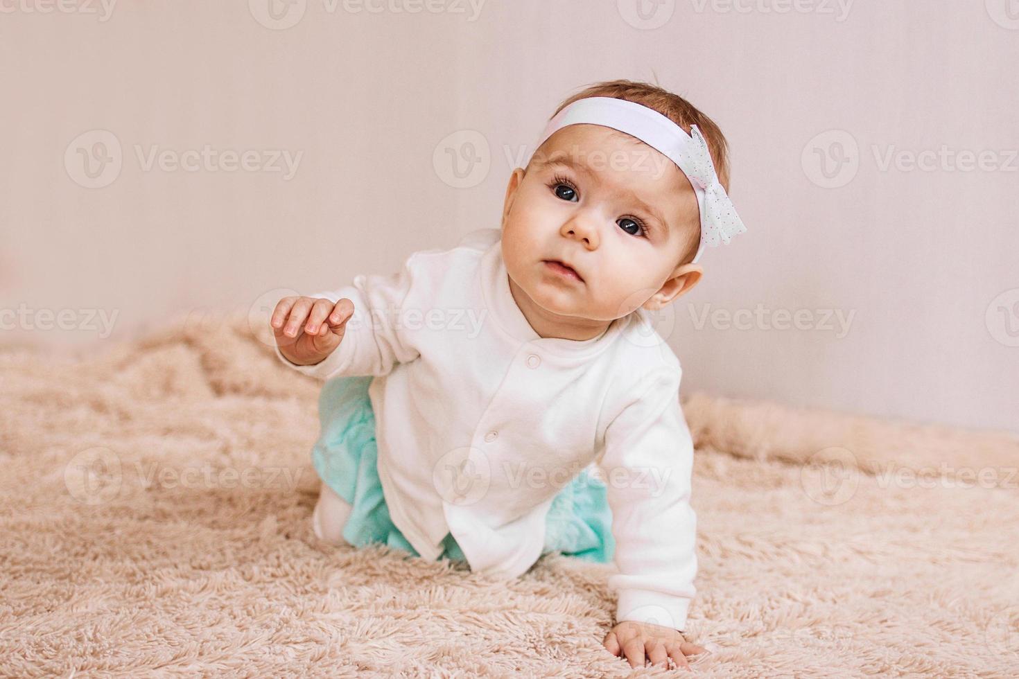 schattig weinig meisje in blauw en wit jurk is zittend Aan een beige pluche plaid. foto