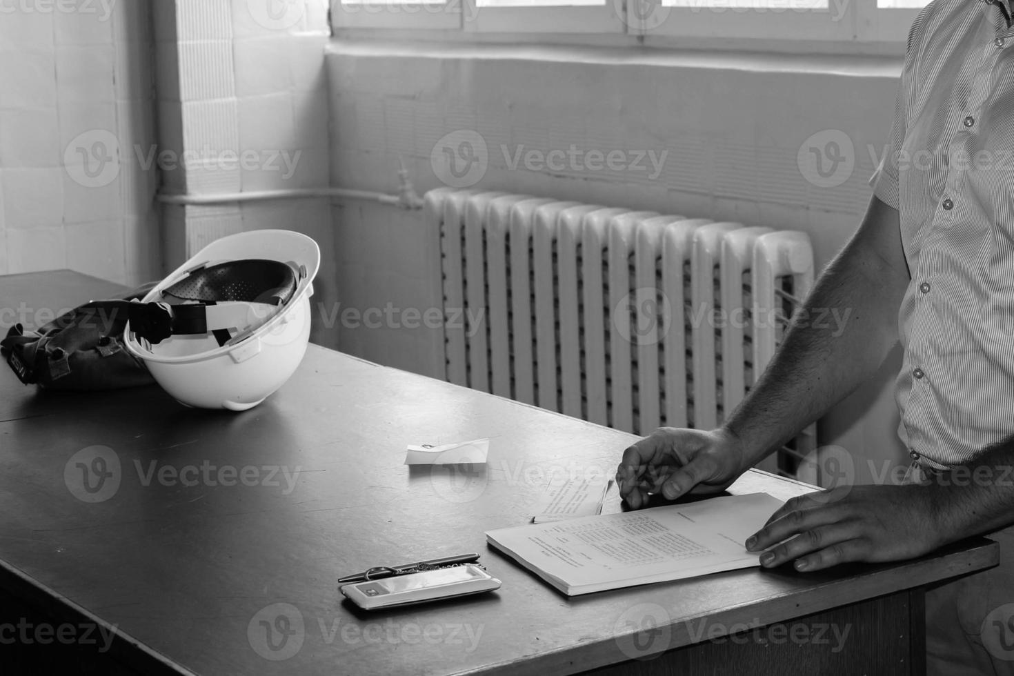 een Mens werken ingenieur met een wit helm Aan de bureau leert naar schrijven in een notitieboekje foto