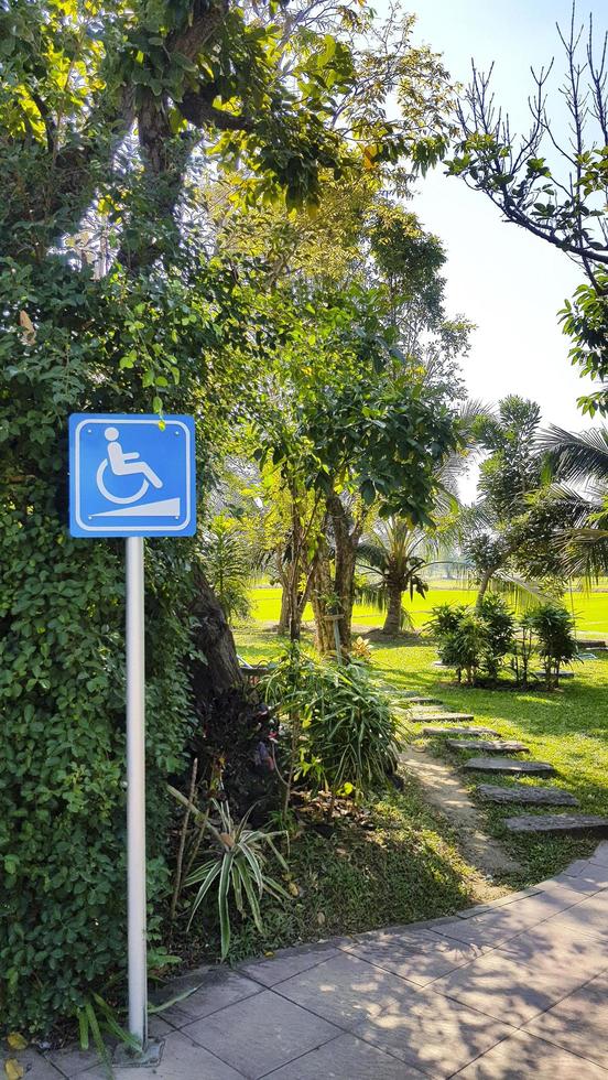 blauw uithangbord, teken of symbool voor gehandicapt rolstoelen naar vertellen richting en manier naar krijgen omhoog cafe winkel met traject en tuin park achtergrond. foto