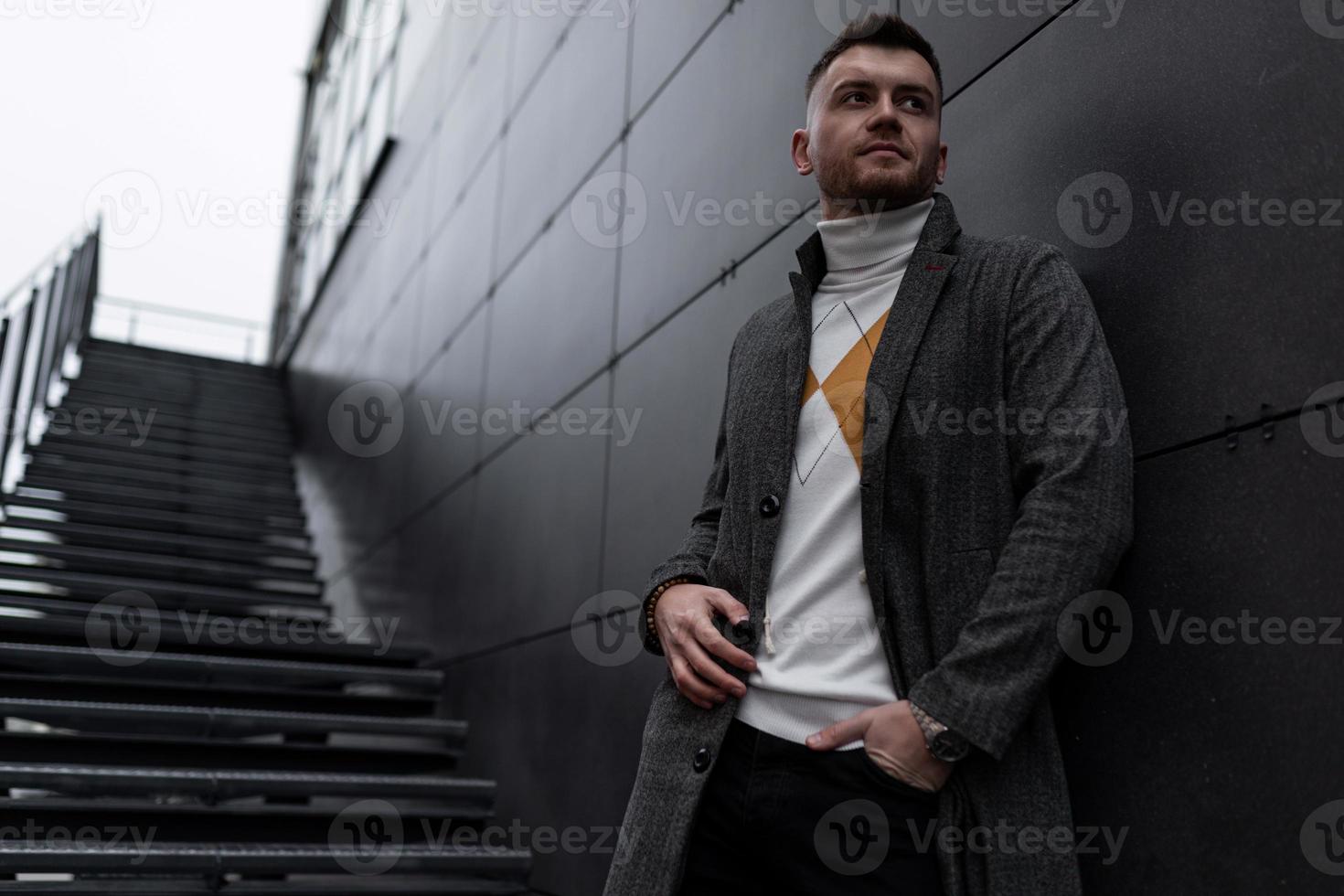 elegant portret van een brutaal Mens Aan de achtergrond van een modern grijs gebouw foto