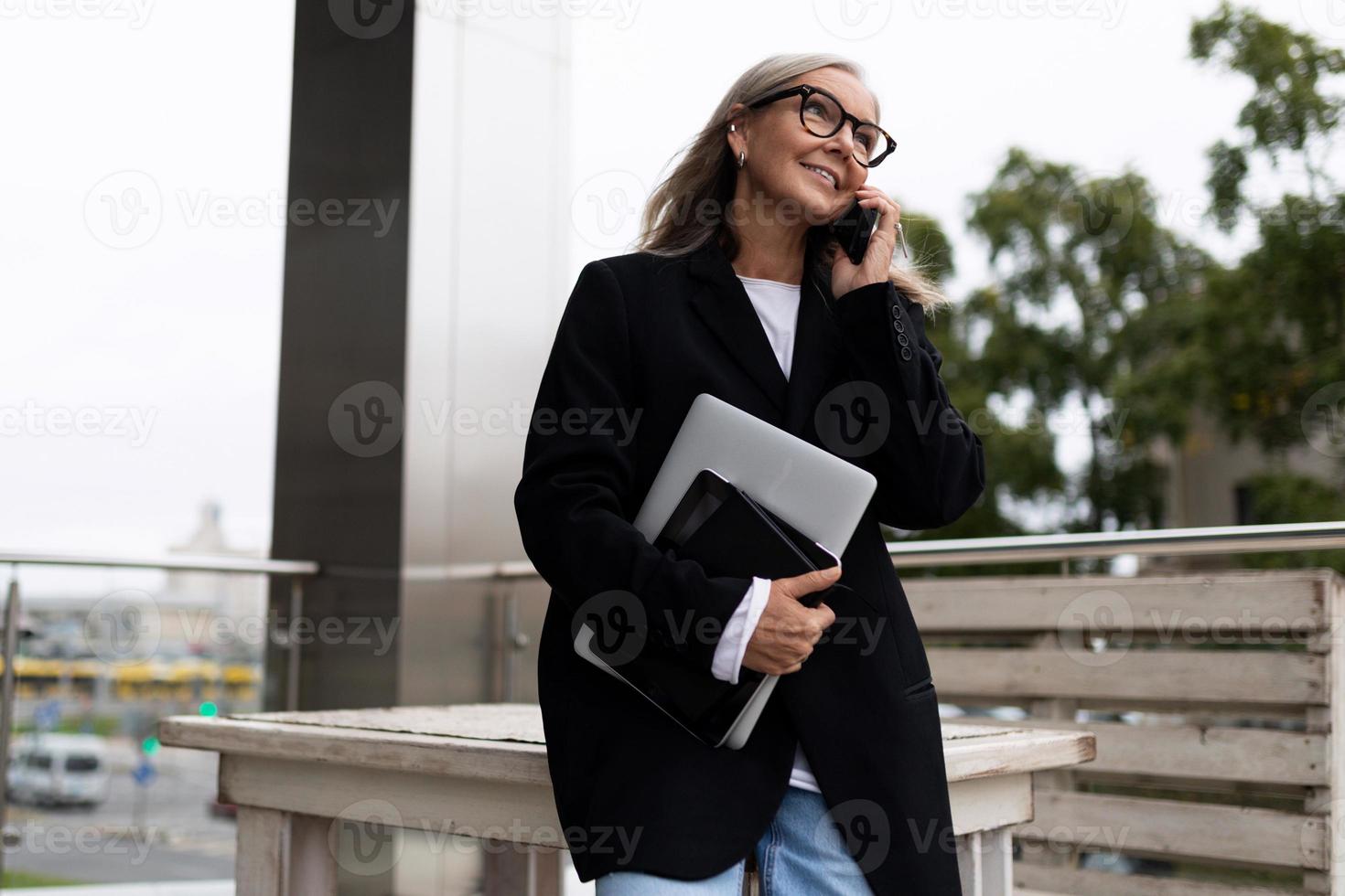 portret van een geslaagd bedrijf ouderen zakenman met een laptop in zijn handen pratend Aan een mobiel telefoon foto