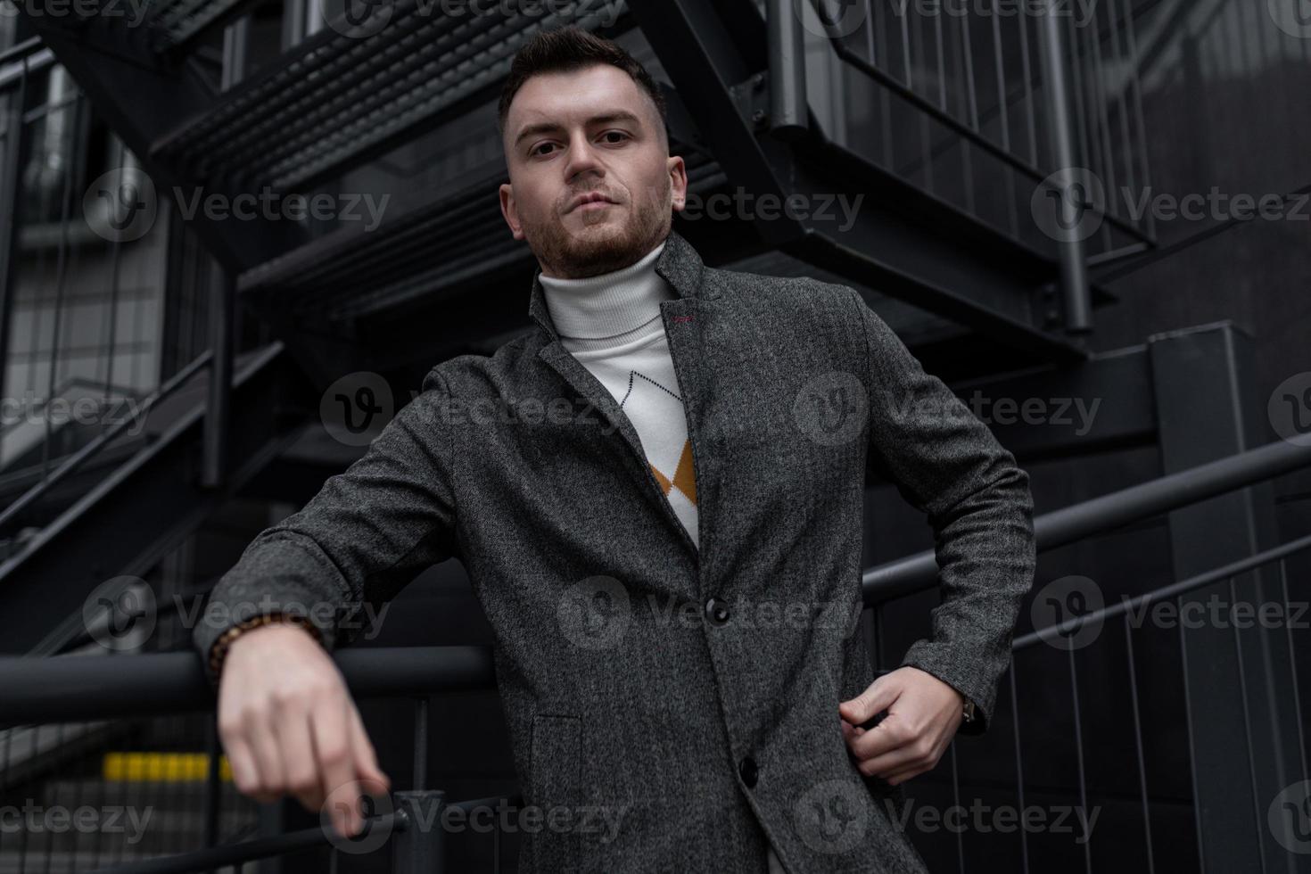 elegant portret van een brutaal Mens in een jas Aan de achtergrond van een zwart gebouw foto