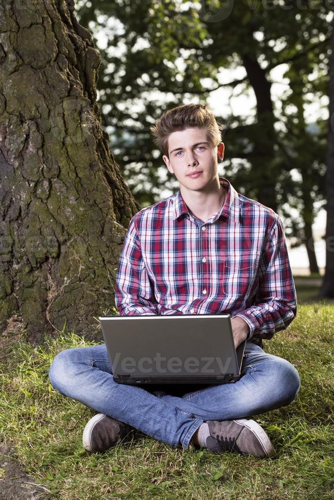 jonge jongen in een park met laptop foto