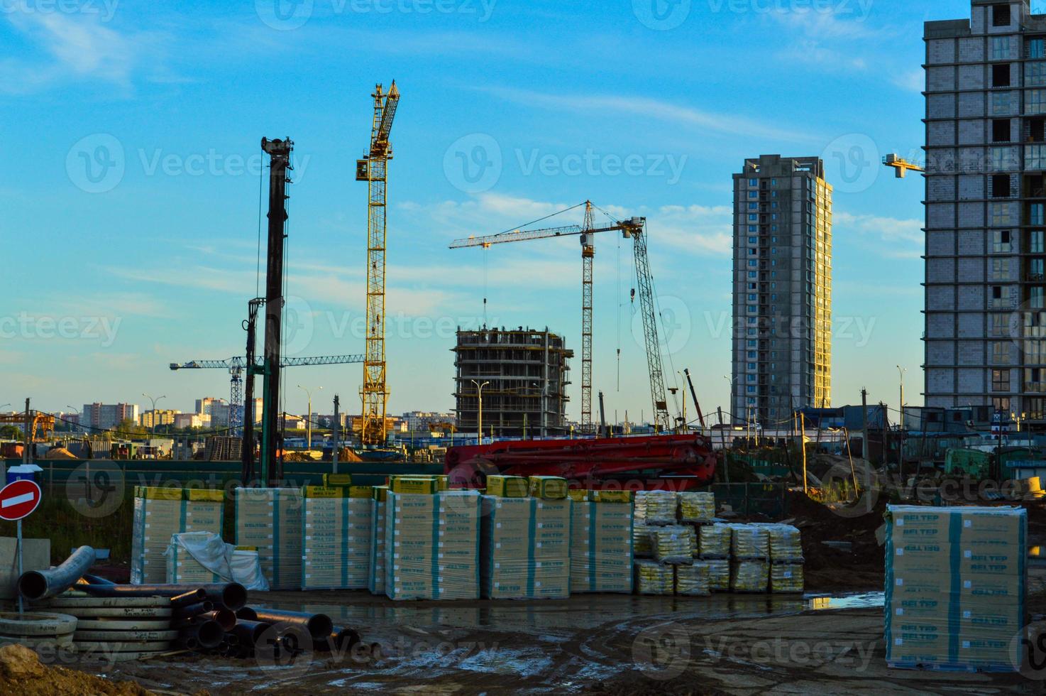 bouw plaats in de stad centrum. gebouw materialen zijn opgestapeld in een stapel onder de film. huizen gebouwd in de afstand, bouw kranen zijn staan. in de centrum van een plas na regenen, modder foto