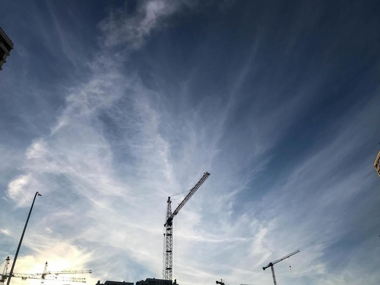 bouw kranen staan tegen de achtergrond van een bewolkt blauw lucht. bouw plaats, huis gebouw apparatuur. Bouwers rechtop staan hoog huizen van beton blokken foto