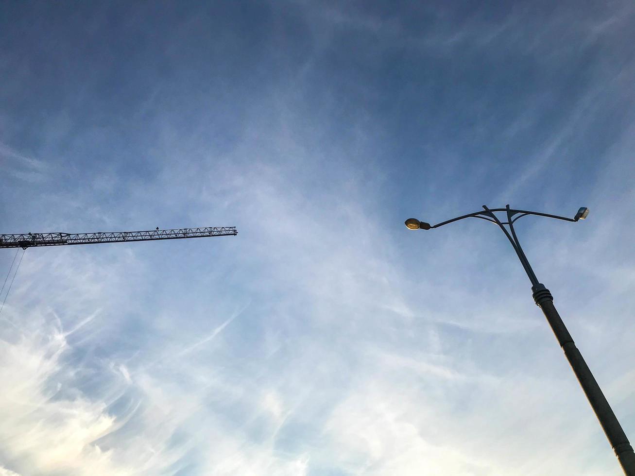 lantarenpaal met een wit licht lamp tegen een Doorzichtig lucht. lantaarn naar verlichten twee wegen. grijs pijler met een lantaarn. Daar is een bouw kraan in de buurt. de lantaarn en de kraan foto