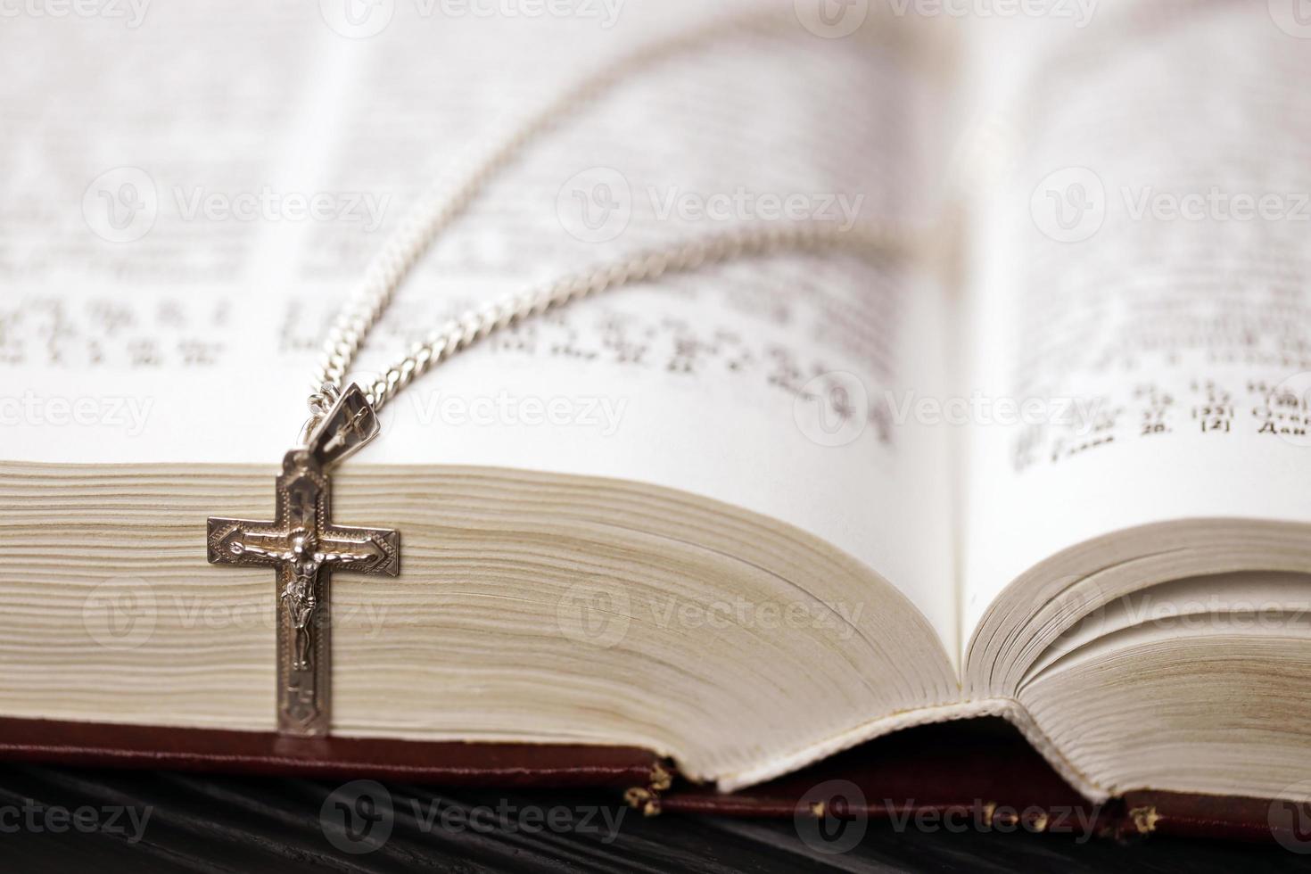 zilver ketting met kruisbeeld kruis Aan christen heilig Bijbel boek Aan zwart houten tafel. vragen zegeningen van god met de macht van heiligheid, welke brengt geluk foto