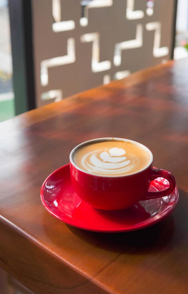 dichtbij omhoog rood koffie kop met hart vorm latte kunst Aan hout tafel foto