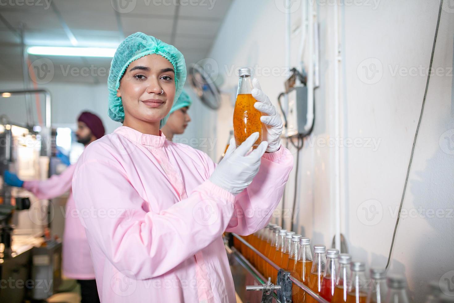 Aziatisch vrouw arbeider is controle Product flessen van fruit sap Aan de productie lijn in de drank fabriek. fabrikant cheques kwaliteit van voedsel industrie. foto