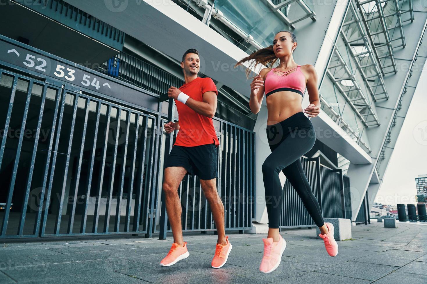 vol lengte van twee zelfverzekerd atleten in sport- kleding rennen terwijl beoefenen buitenshuis foto