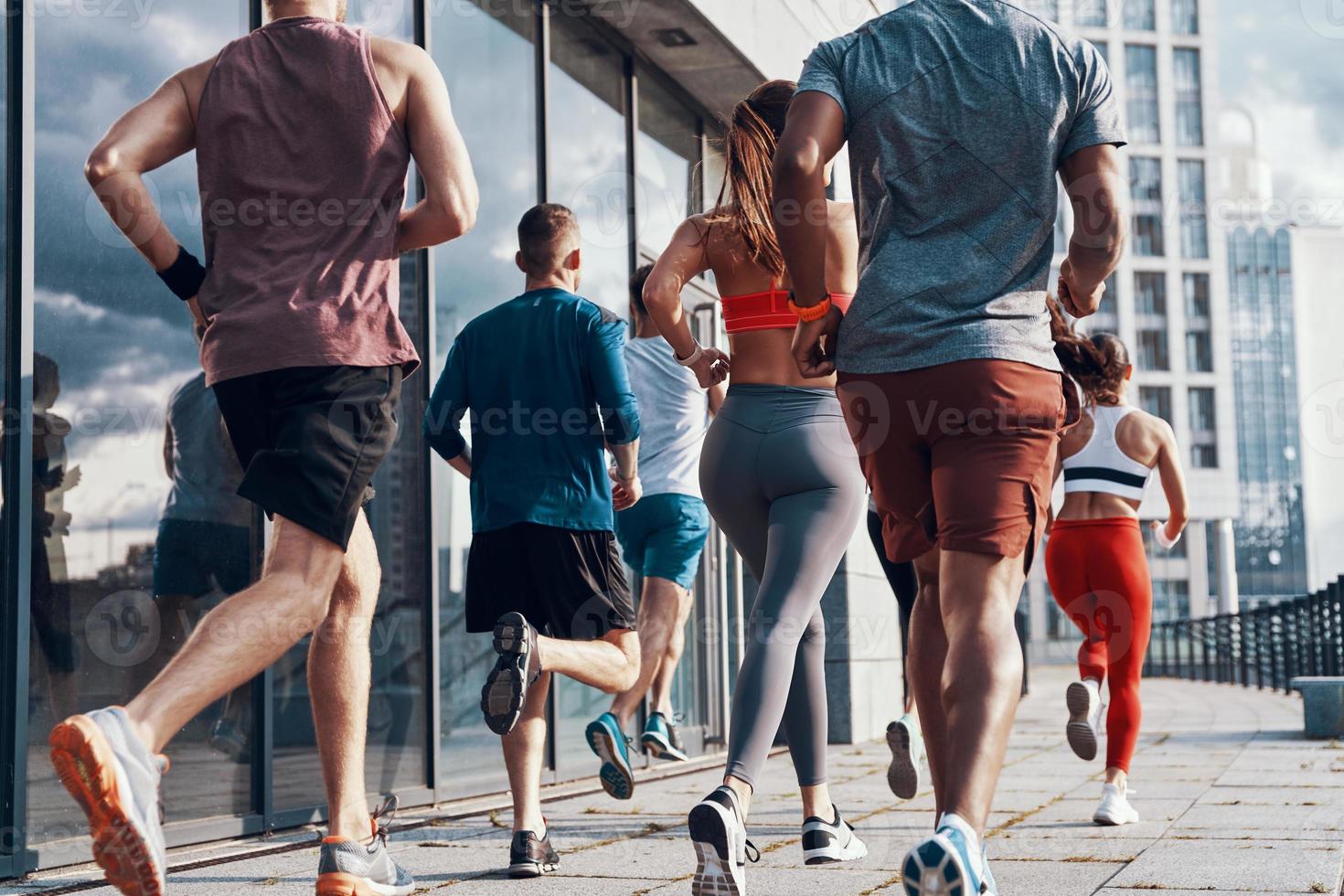 achterzijde visie van mensen in sport- kleding jogging terwijl oefenen Aan de trottoir buitenshuis foto