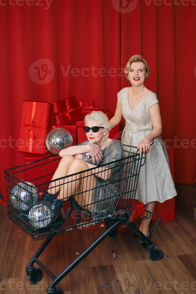 volwassen vrouw rollend elegant senior vrouw in zonnebril en zilver jurk de supermarkt kar Bij de feest. partij, disco, viering, senior leeftijd concept foto