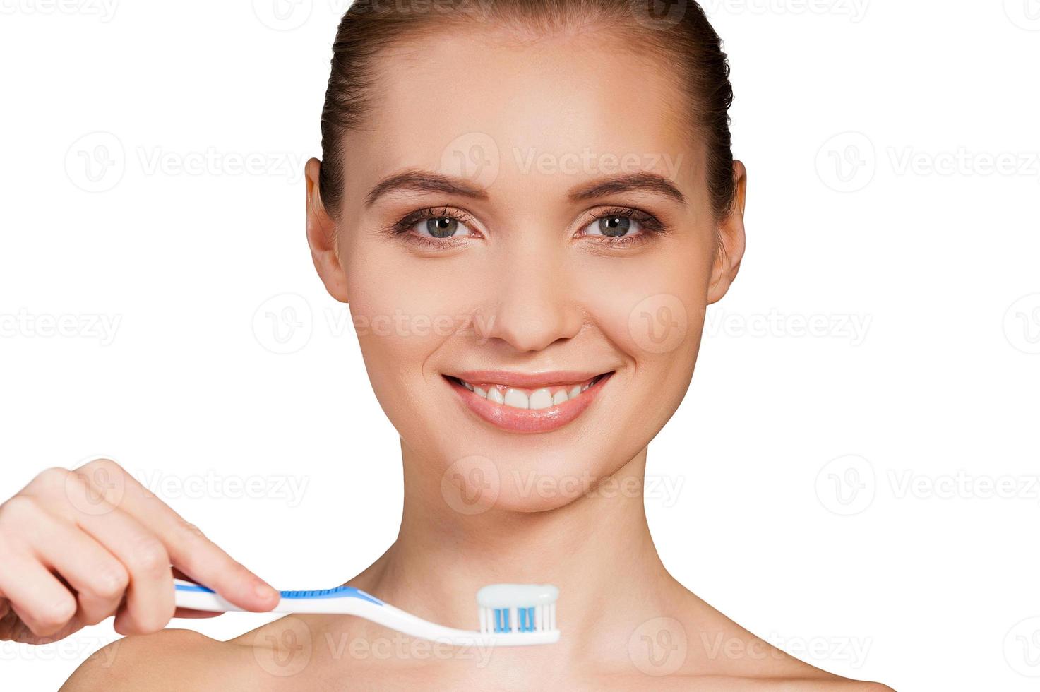 vrouw poetsen tanden. mooi jong vrouw Holding tandenborstel met tandpasta en glimlachen Bij camera terwijl geïsoleerd Aan wit achtergrond foto