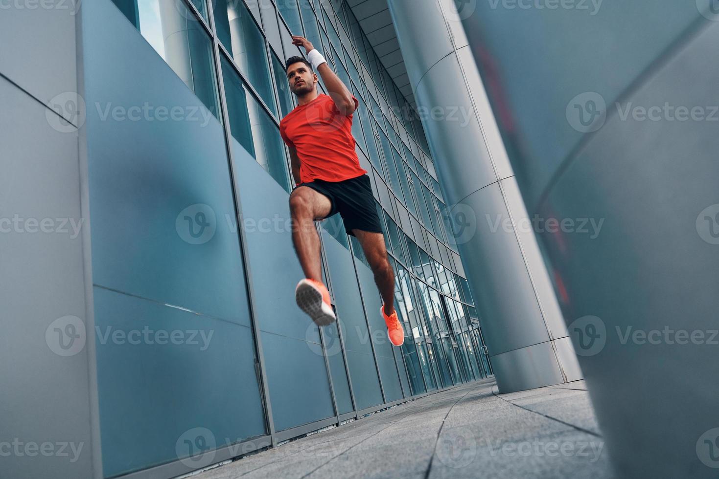 vol lengte van zelfverzekerd jong Mens in sport- kleding zweven in lucht terwijl oefenen buitenshuis foto