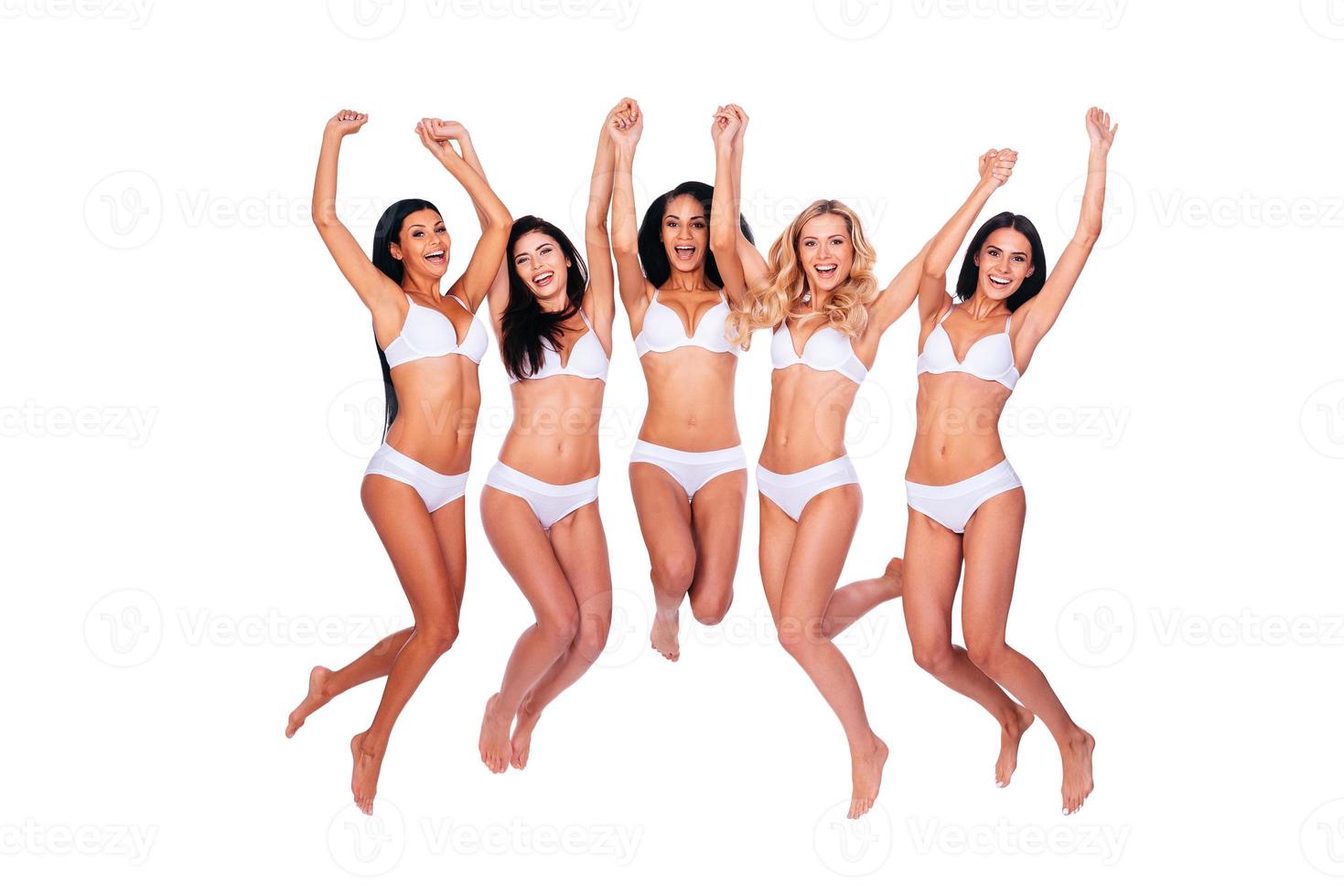 vliegend schoonheden. vol lengte van vijf mooi Dames in lingerie jumping en houden armen verheven tegen wit achtergrond foto