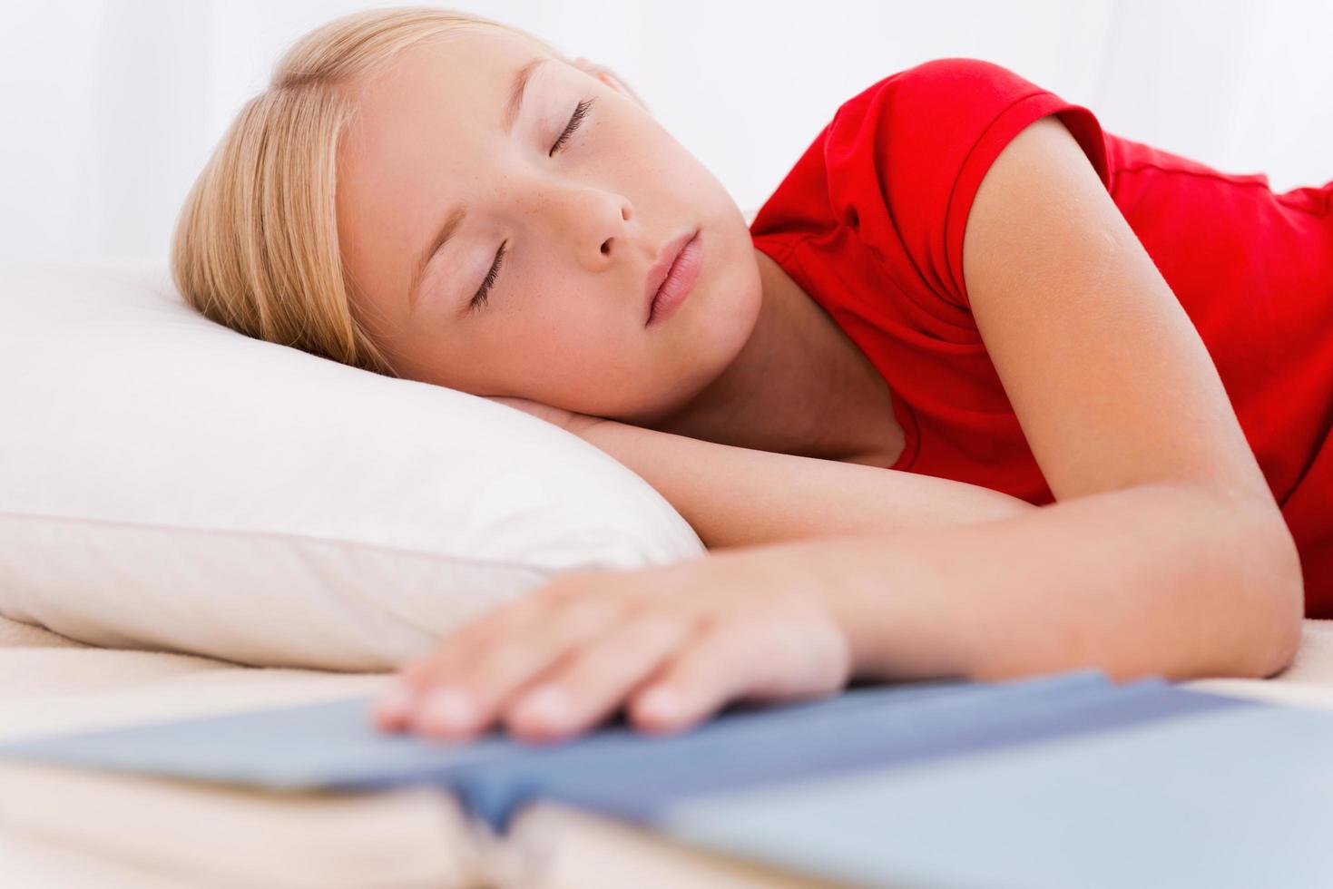 weinig boekenwurm. schattig weinig meisje slapen terwijl aan het liegen in bed en Holding hand- Aan boek foto