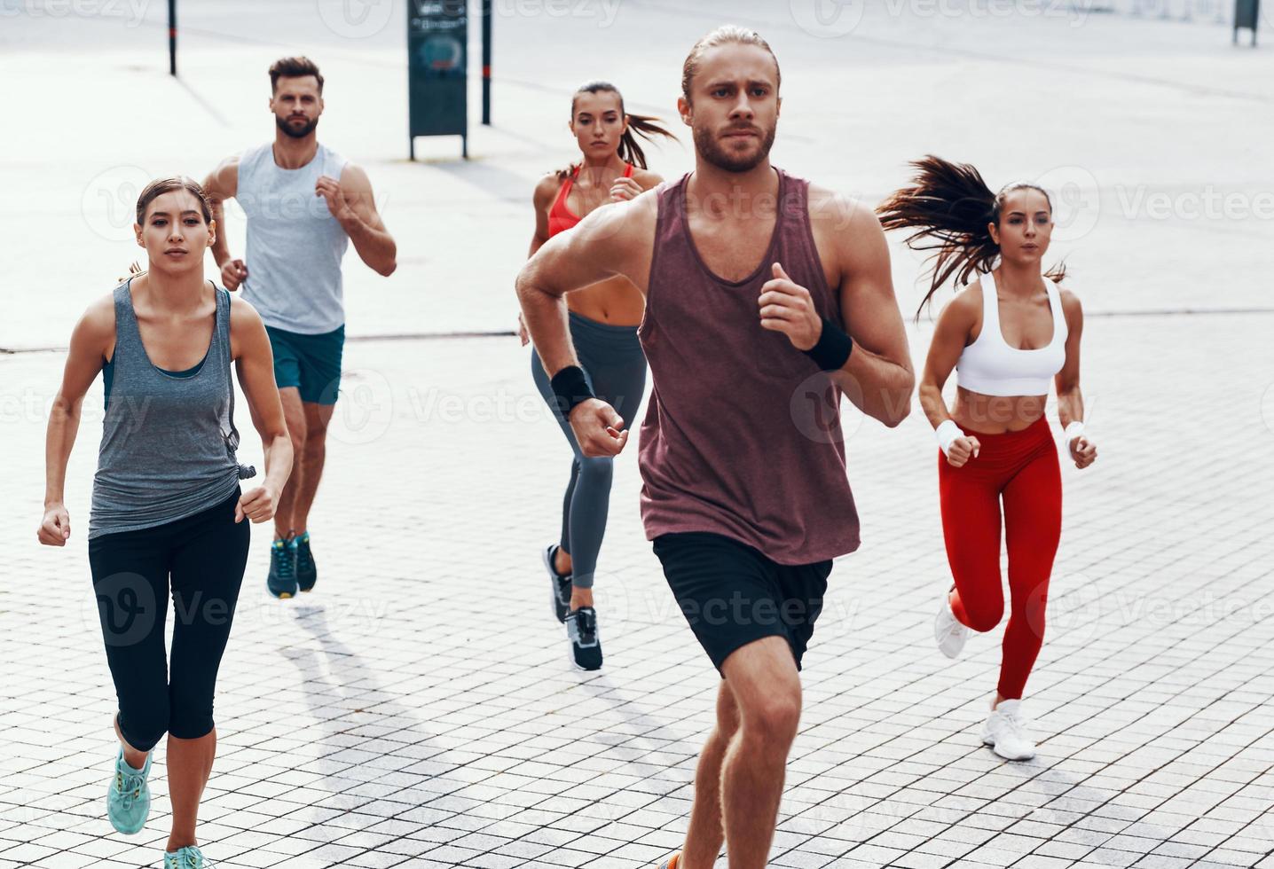 groep van jong mensen in sport- kleding jogging terwijl oefenen Aan de trottoir buitenshuis foto