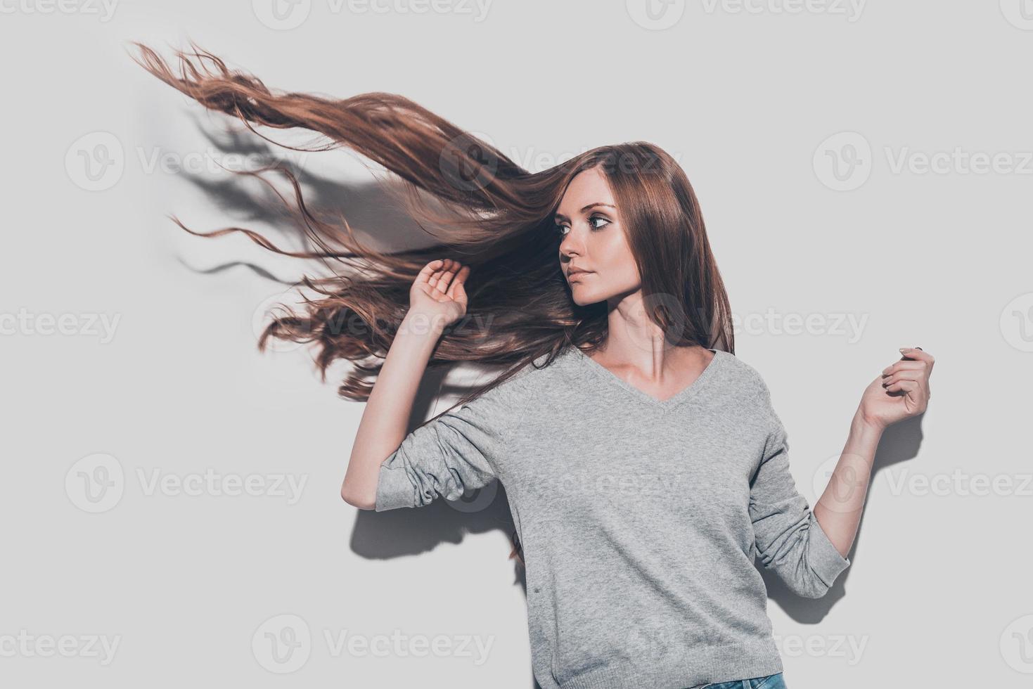 Leuk vinden een brand. aantrekkelijk jong vrouw met verward haar- op zoek weg terwijl staand tegen grijs achtergrond foto