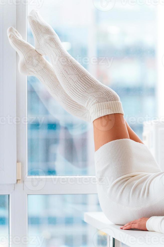 schoonheid in warm sokken. detailopname van vrouw in wit warm sokken houden haar voeten omhoog terwijl aan het liegen in voorkant van de venster Bij huis foto