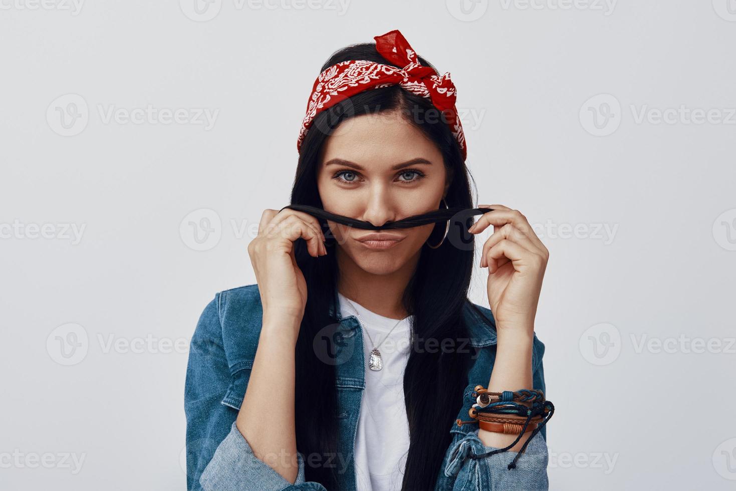 aantrekkelijk jong vrouw in bandana maken een gezicht terwijl staand tegen grijs achtergrond foto