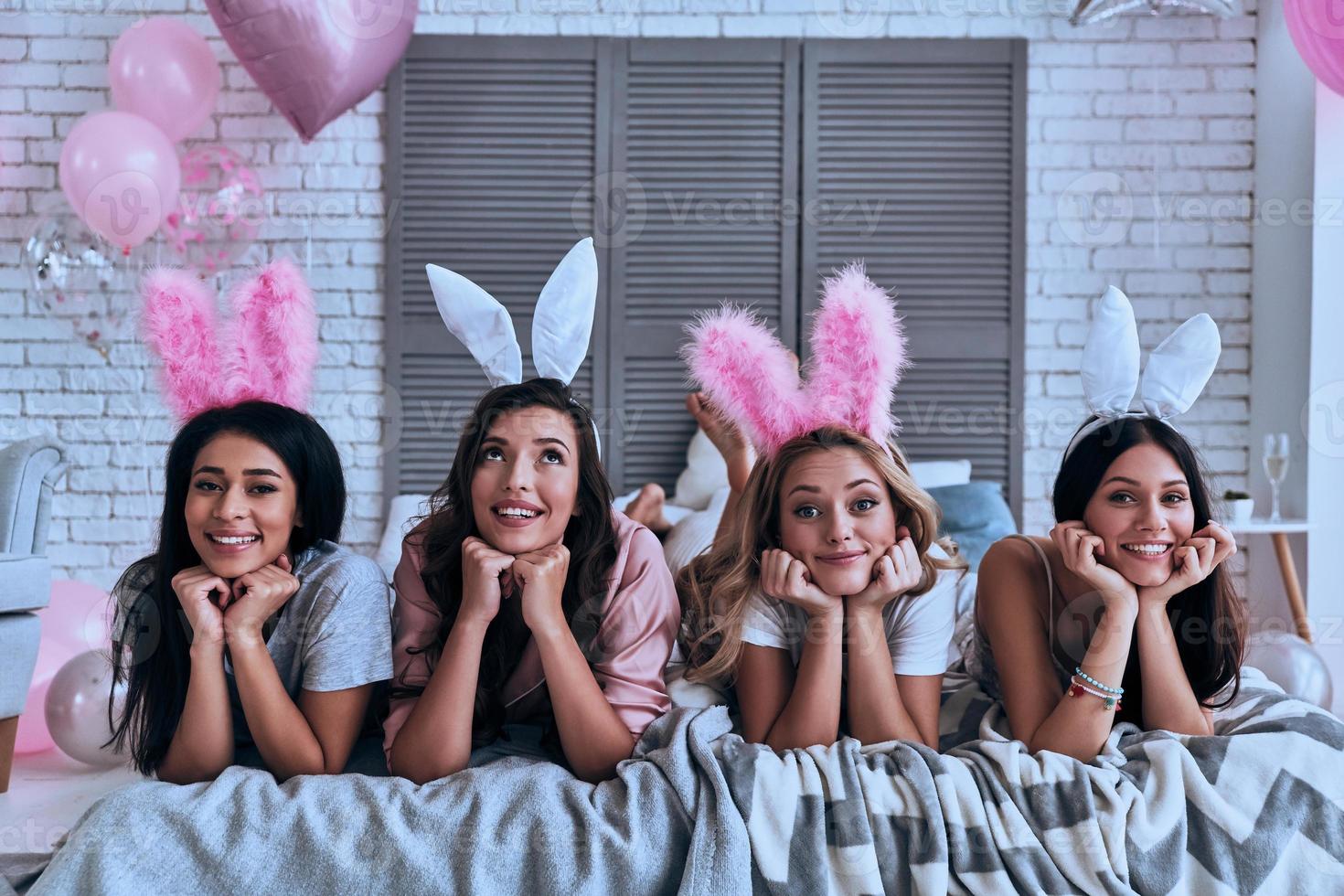 zuiver schoonheden. vier aantrekkelijk jong Dames in konijn oren glimlachen terwijl aan het liegen Aan de bed foto