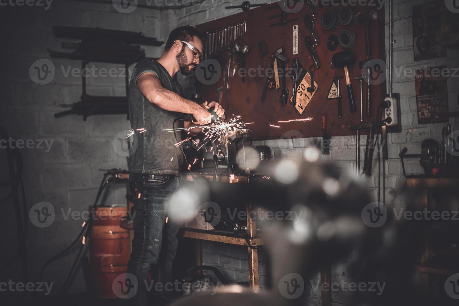 werk voor echt Heren. zelfverzekerd jong Mens slijpen met vonken in reparatie winkel foto