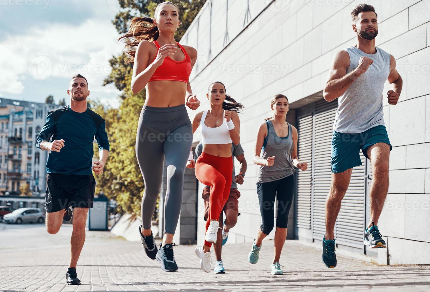 vol lengte van mensen in sport- kleding jogging terwijl oefenen Aan de trottoir buitenshuis foto