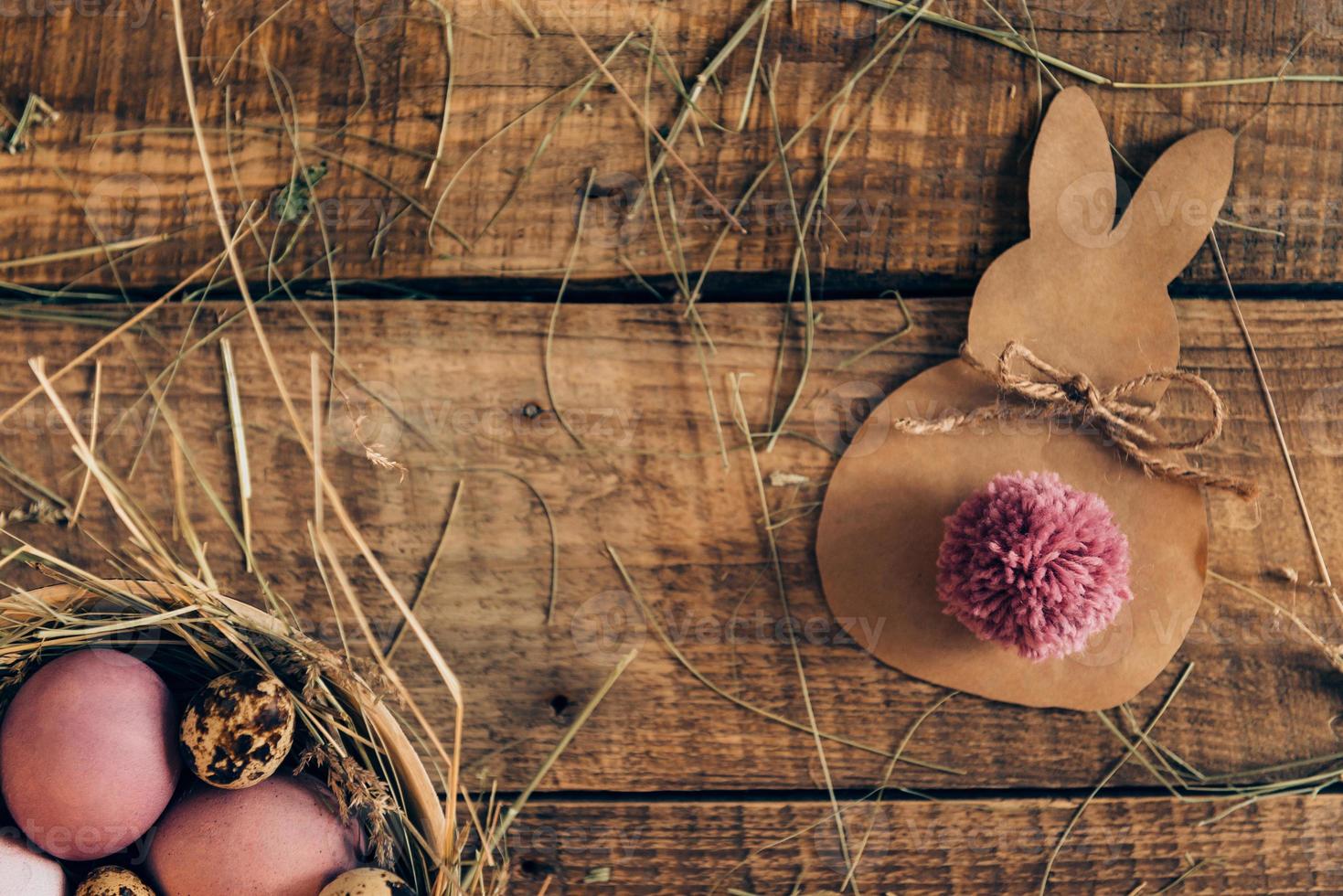 ester konijn. top visie van gekleurde Pasen eieren in kom met hooi en Pasen konijn gemaakt van bruin papier aan het liegen Aan houten rustiek tafel foto