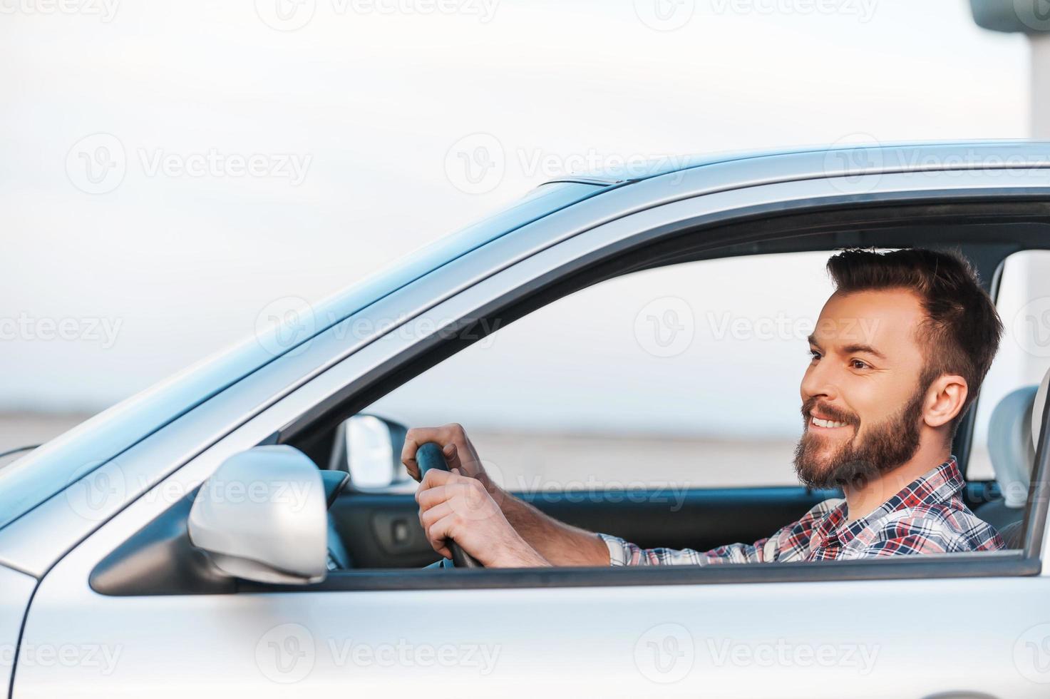 rijden zijn nieuw auto. kant visie van knap jong Mens het rijden zijn auto en glimlachen foto