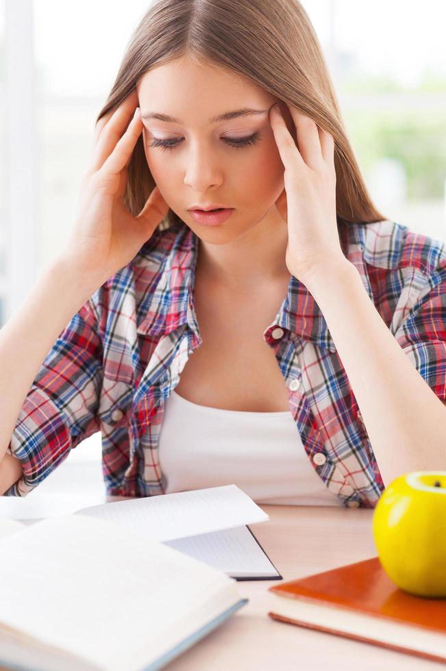 gevoel uitgeput. gefrustreerd tiener- meisje Holding hoofd in handen terwijl zittend Bij de bureau met boeken houdende Aan het foto