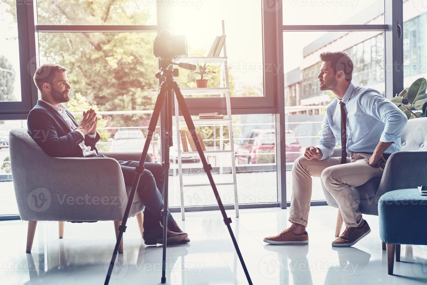 filmen interview. twee jong mannen in slim gewoontjes slijtage pratend terwijl maken nieuw video binnenshuis foto