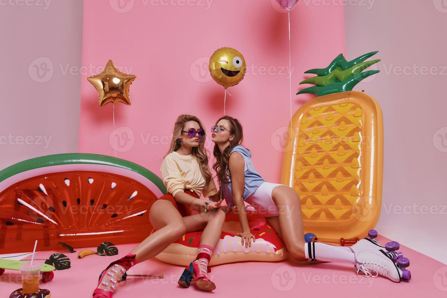 resting samen. twee mooi jong Dames glimlachen terwijl zittend Aan de opblaasbaar ring tegen roze achtergrond foto