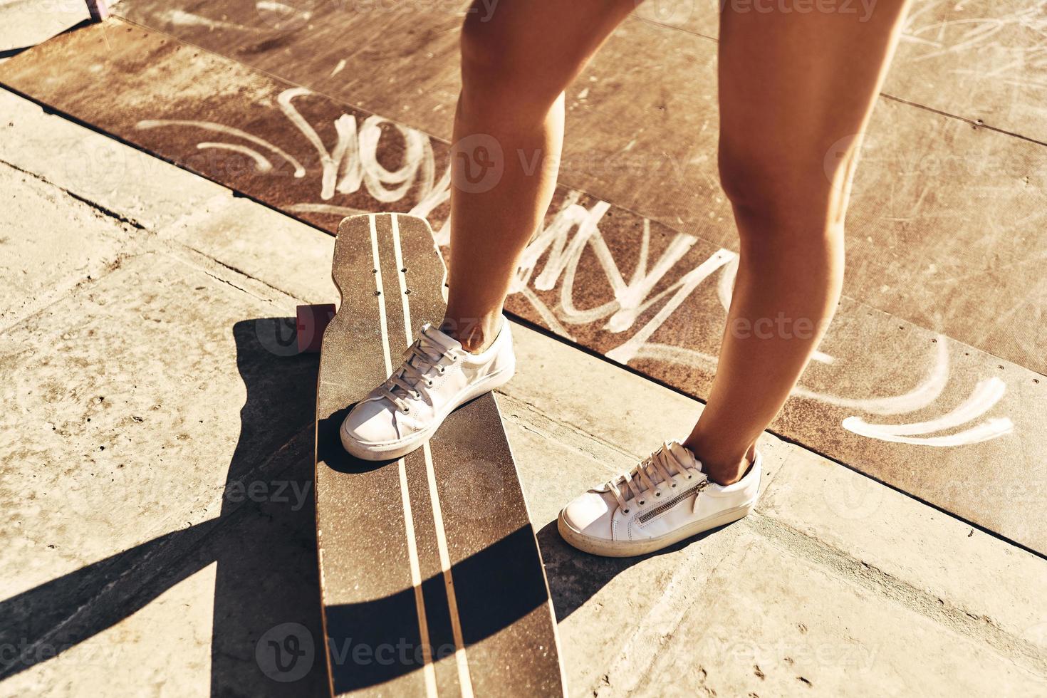 genieten van elke minuut van zomer. detailopname van jong vrouw houden een voet Aan de skateboard terwijl uitgeven tijd buitenshuis foto