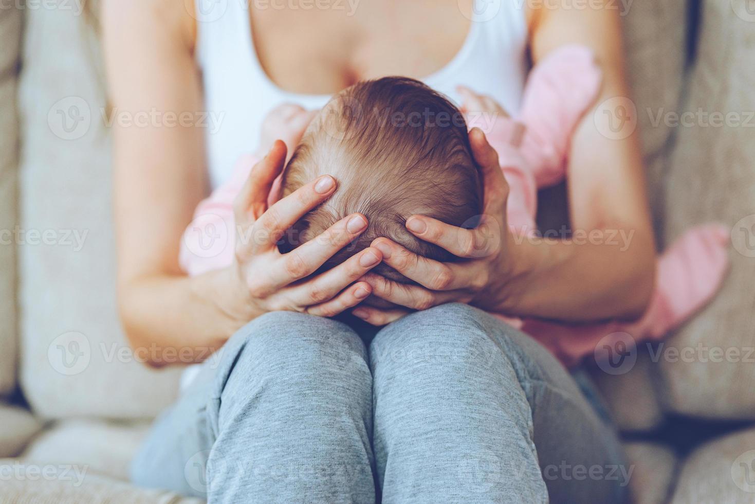 schat in haar handen. dichtbij omhoog een deel van jong vrouw Holding baby meisje Aan haar knieën terwijl zittend Aan de bankstel foto