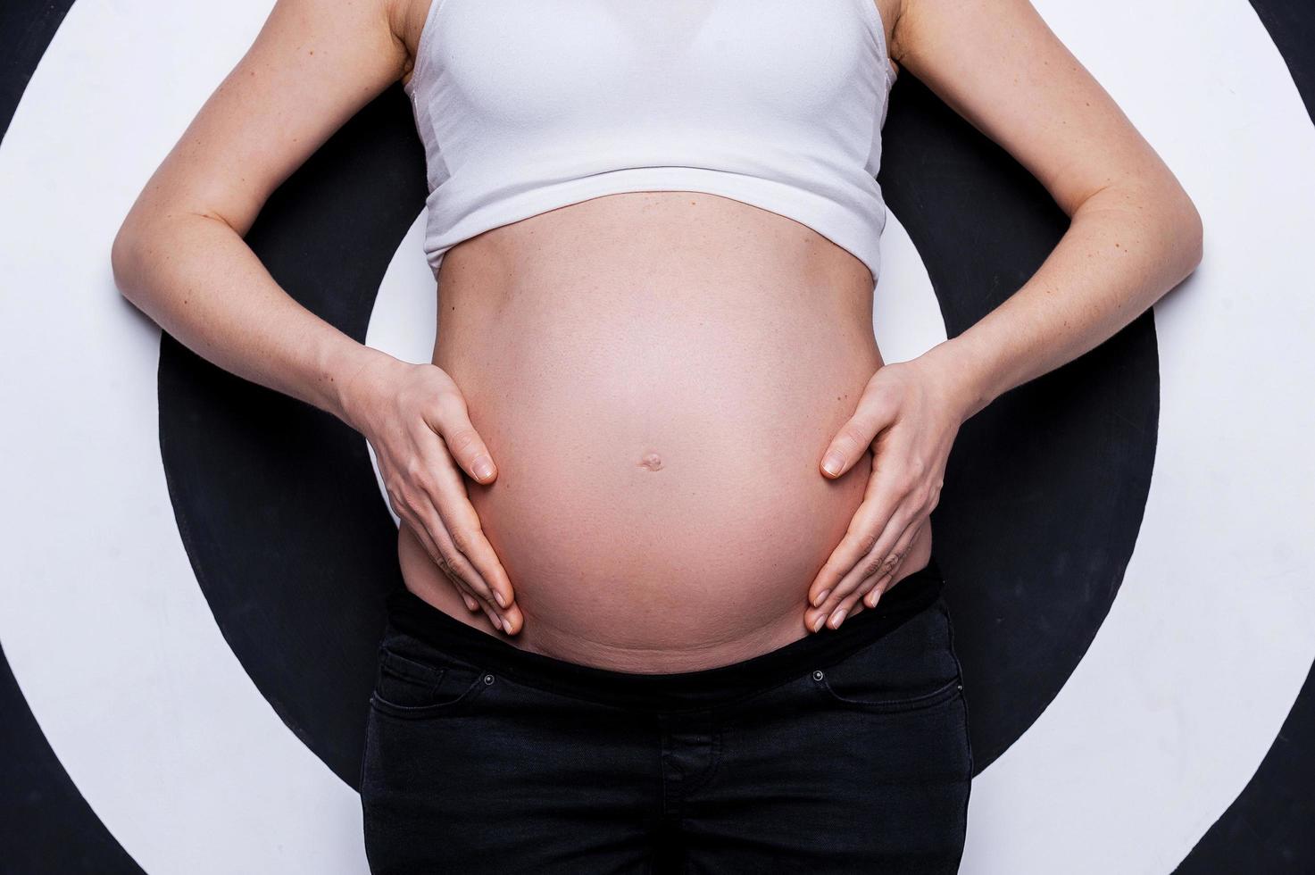 zwanger buik. bijgesneden beeld van zwanger vrouw Holding handen Aan buik terwijl staand tegen doelwit achtergrond foto