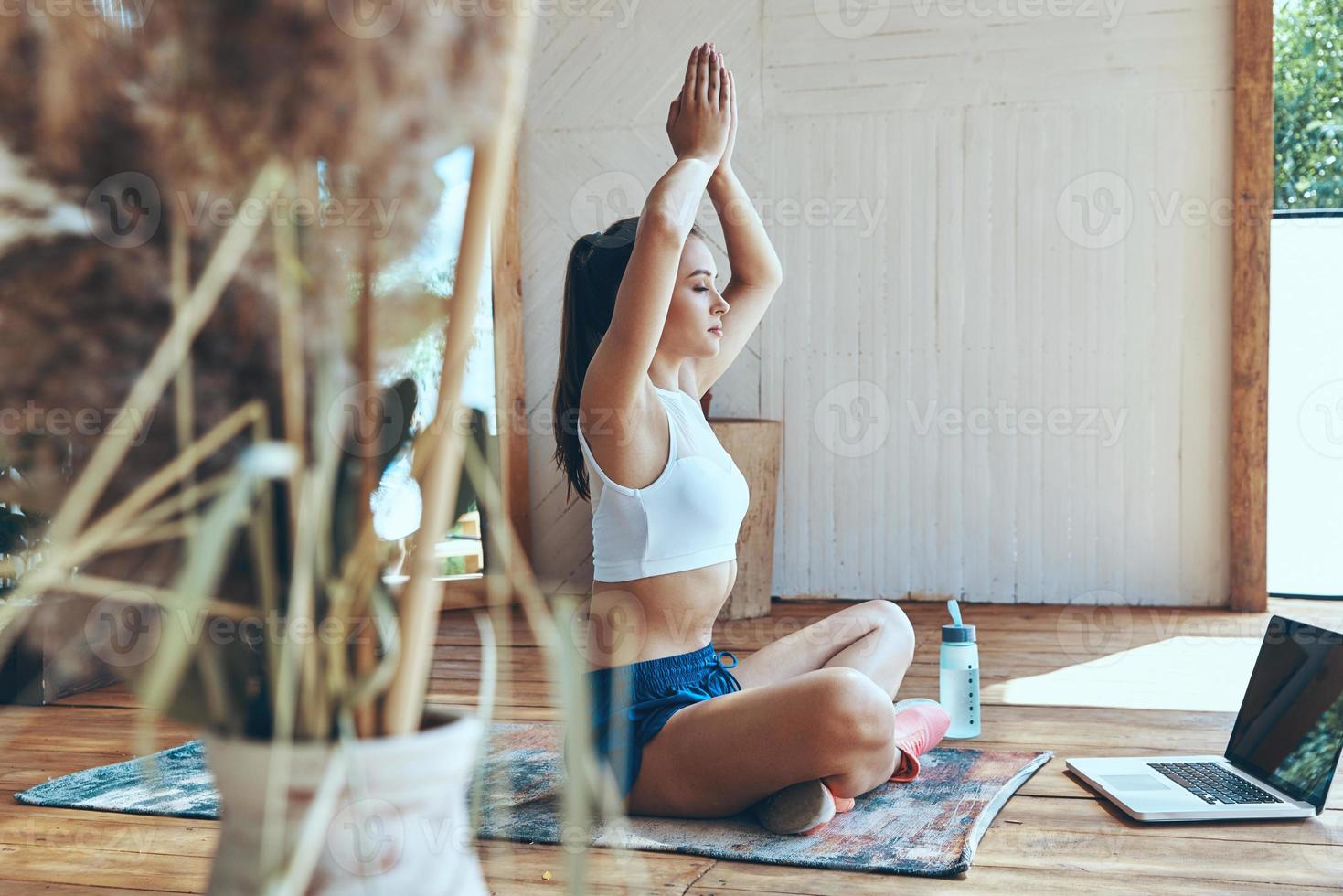 mooi jong vrouw in sport- kleding beoefenen yoga Aan patio met laptop houdende in de buurt haar foto