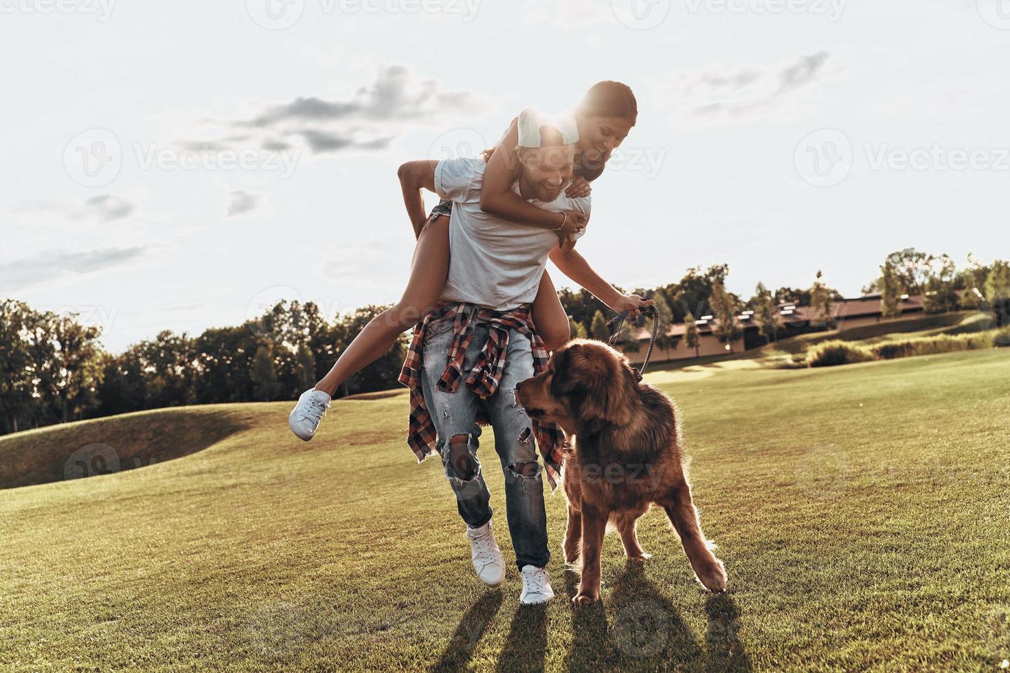 totaal in liefde. vol lengte van knap jong Mens draag- jong aantrekkelijk vrouw Aan schouders terwijl wandelen met hun hond buitenshuis foto