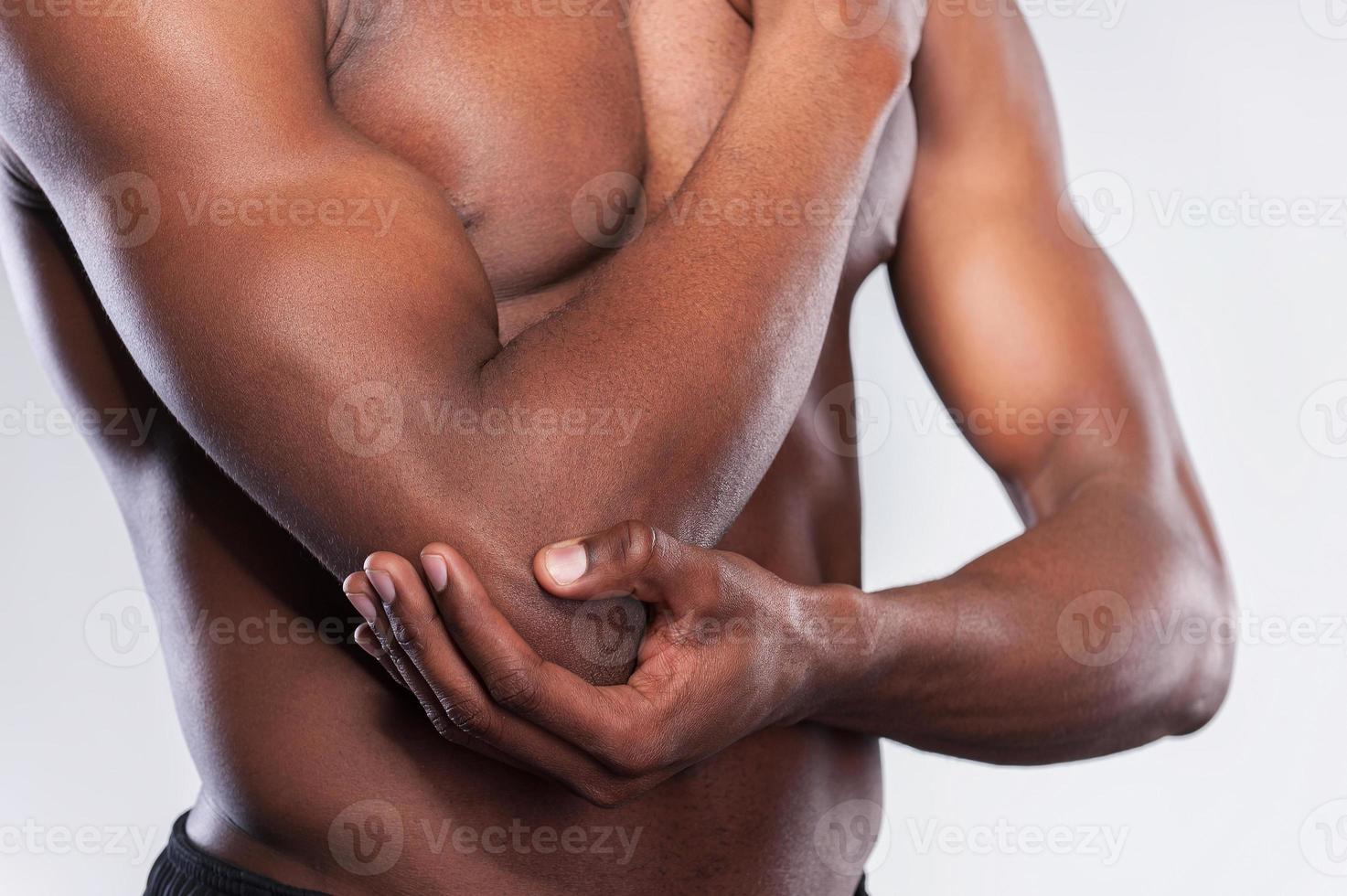 pijn in elleboog. bijgesneden beeld van jong gespierd Afrikaanse Mens aanraken zijn elleboog terwijl staand tegen grijs achtergrond foto