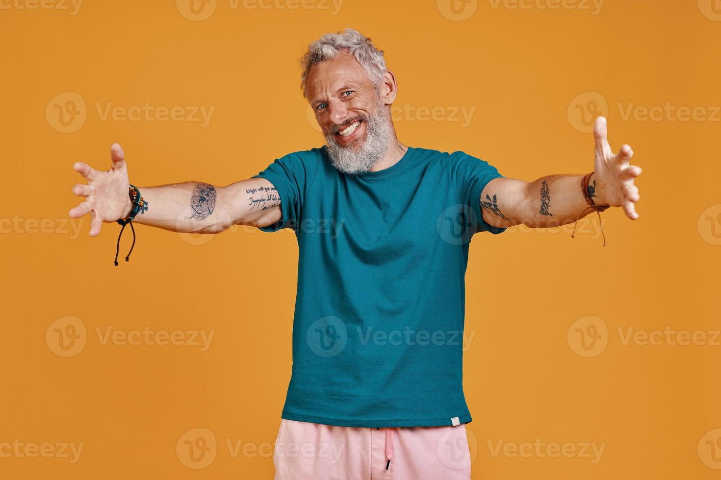 gelukkig senior Mens houden armen uitgestrekt en glimlachen terwijl staand tegen oranje achtergrond foto