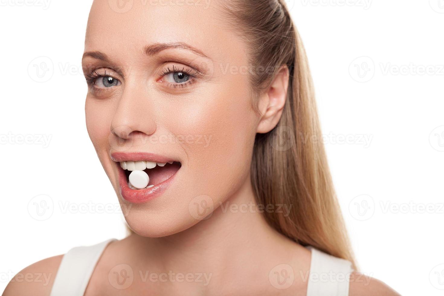 pil in haar mond. portret van de jonge pil van de vrouwenholding in haar mond en het glimlachen terwijl geïsoleerd op wit foto