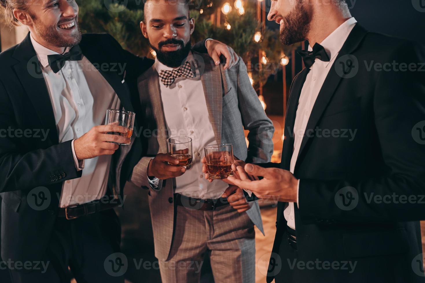 drie goed gekleed mannen drinken whisky en communiceren terwijl uitgeven tijd Aan partij foto