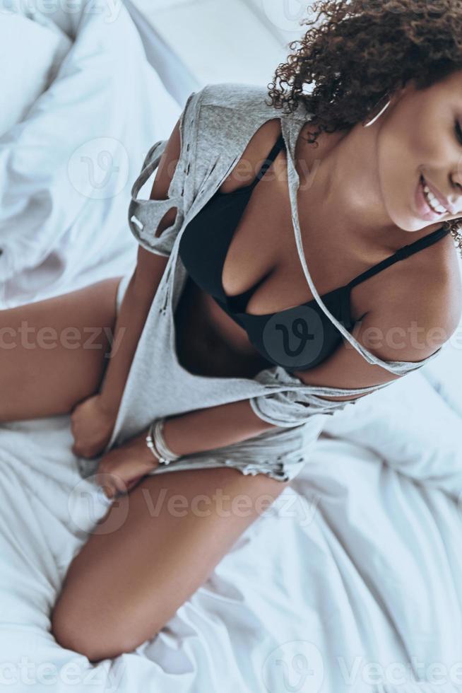 lui schoonheid. detailopname top visie van mooi jong Afrikaanse vrouw in zwart lingerie glimlachen terwijl zittend Aan de bed Bij huis foto