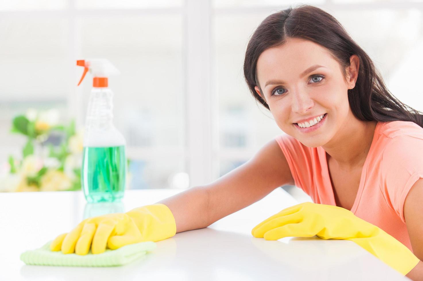 vrolijk huisvrouw. jong mooi vrouw geel handschoenen leunend Bij de tafel en glimlachen foto