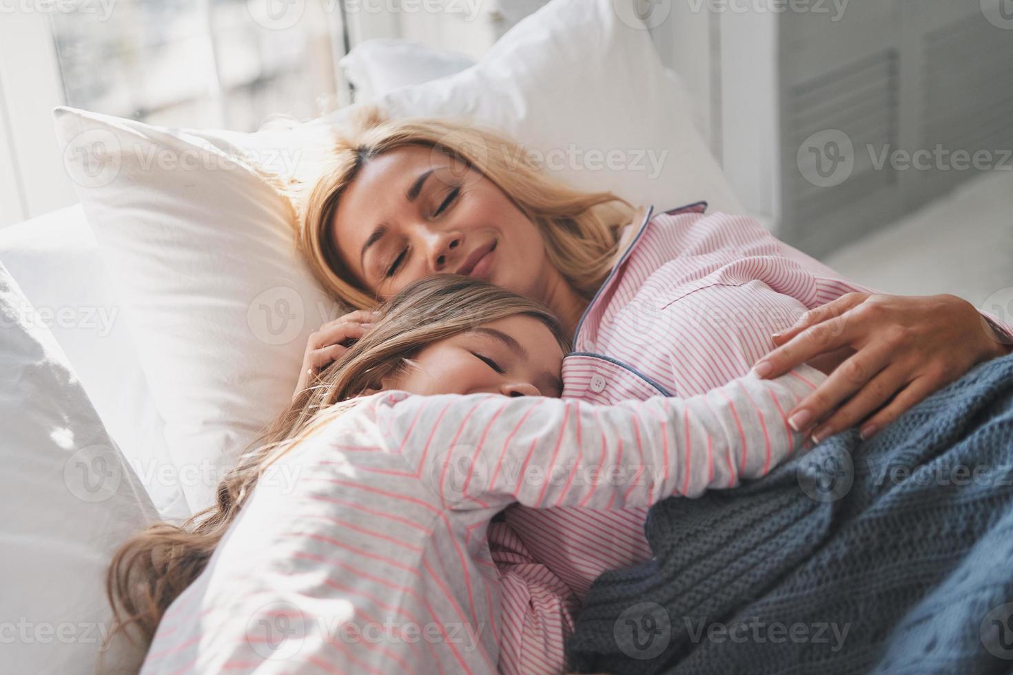 moeder en dochter houden ogen Gesloten en glimlachen terwijl aan het liegen Aan de bed Bij huis foto