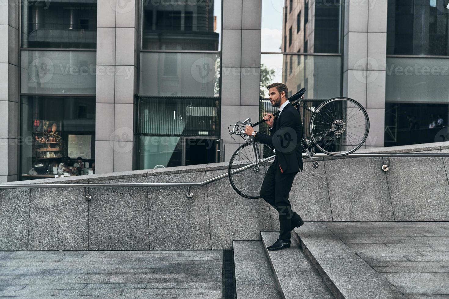 vermijden verkeer. vol lengte van jong Mens in vol pak draag- zijn fiets terwijl wandelen buitenshuis foto