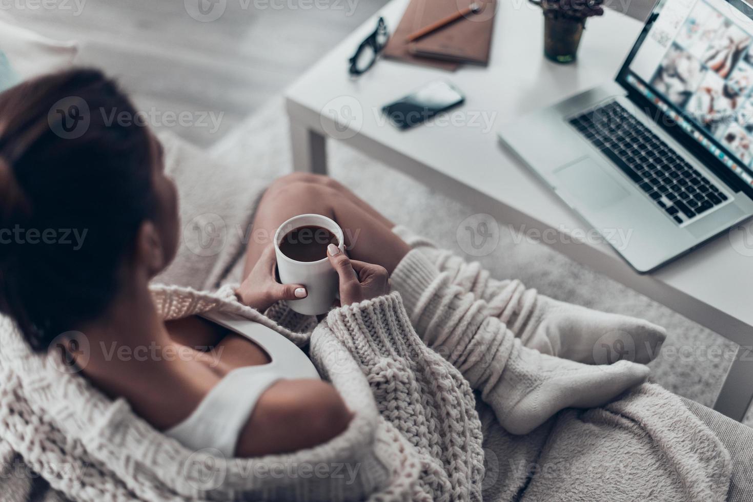 genieten van vers koffie. top visie van mooi jong vrouw Holding kop terwijl ontspannende Aan bankstel Bij huis foto