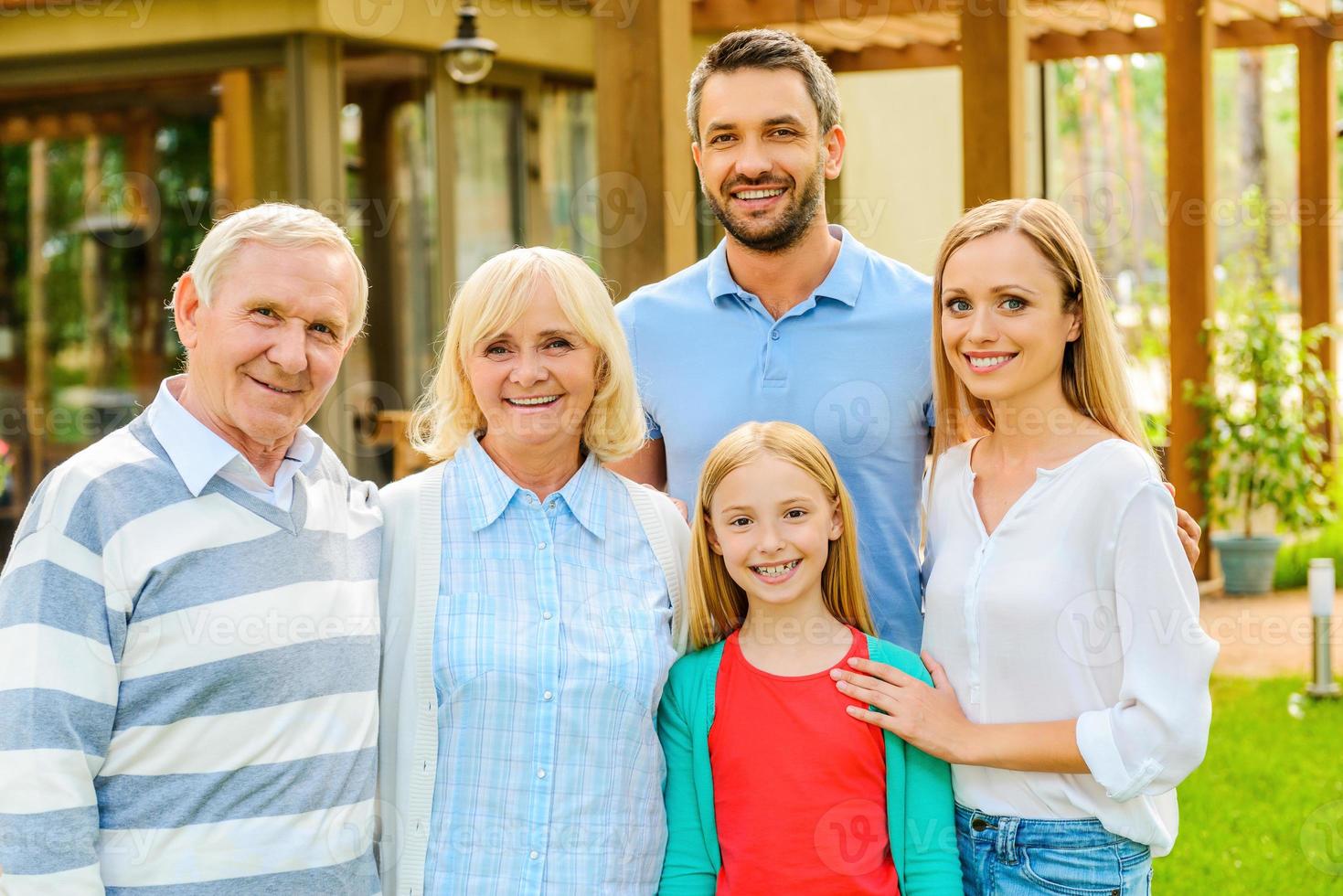 familie bijeenkomst. gelukkig familie van vijf mensen bonding naar elk andere en glimlachen terwijl staand Bij de terug werf van hun huis samen foto